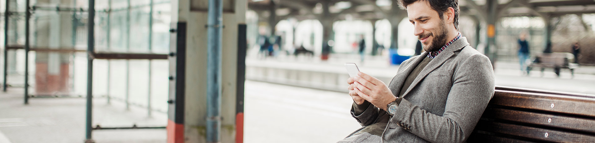 Mann sitzt am Bahnhof auf einer Bank und benutzt ein Smartphone