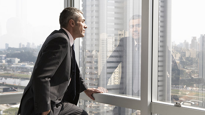 Geschäftsmann, der an einer Fensterfront steht (Getty Images)