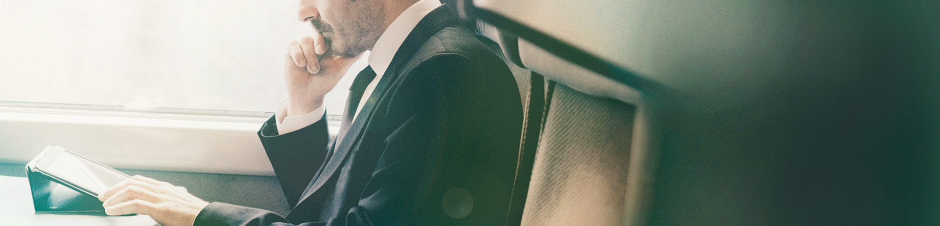 ein Mann im Businessoutfit sitzt in einem Zug und arbeitet auf seinem Tablet